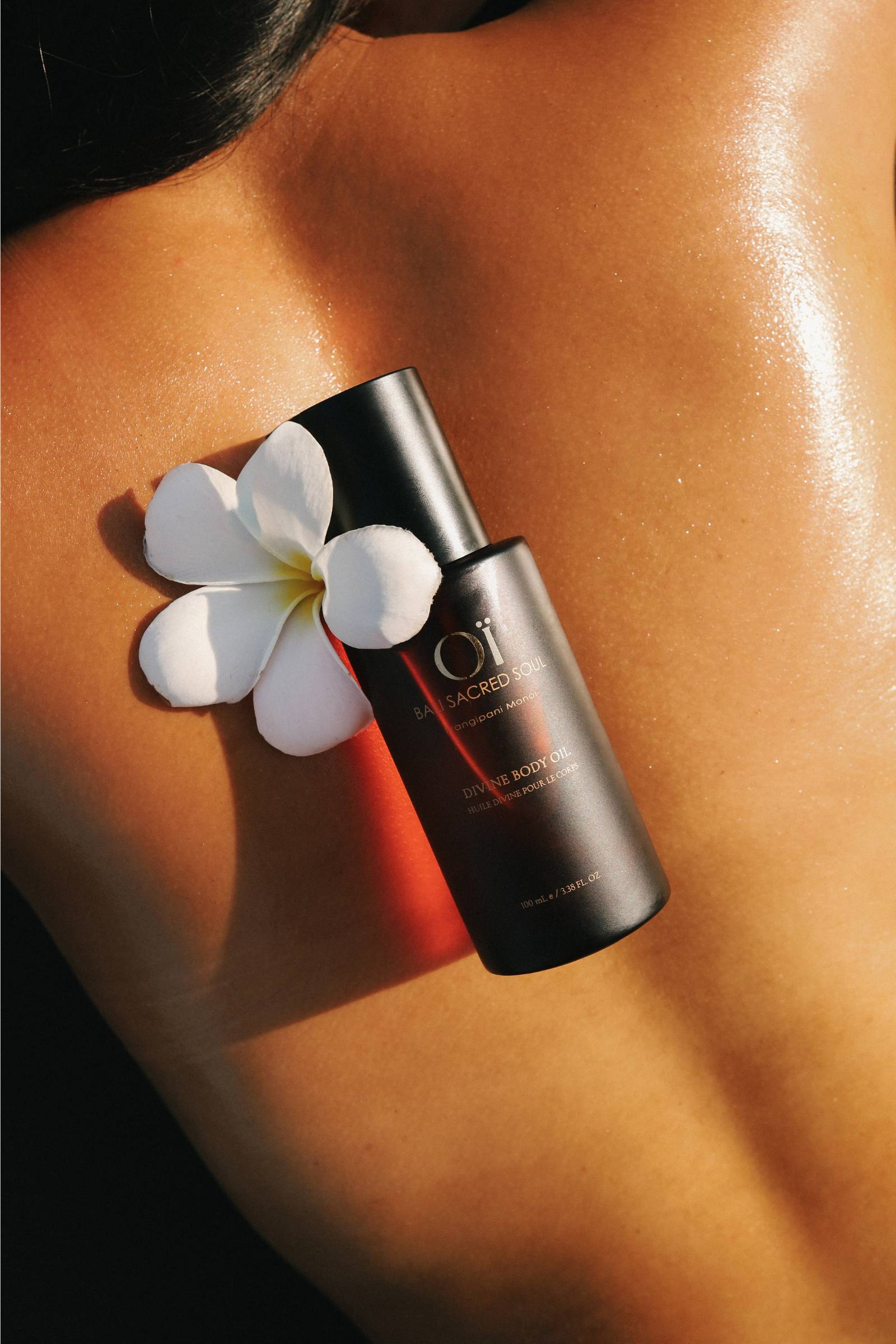 Dos huilé avec des fleurs de frangipanier blanches sable chaud et divine body oil