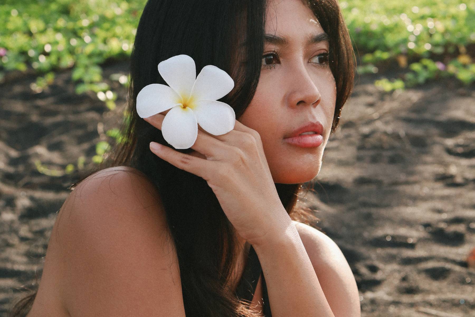 Portrait d'une femme au soleil sur une plage de Bali tenant un fleur de frangipanier